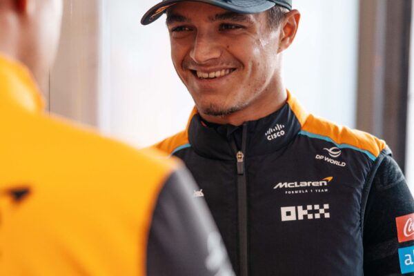 Lando Norris in a McLaren suit, looking over a McLaren employee