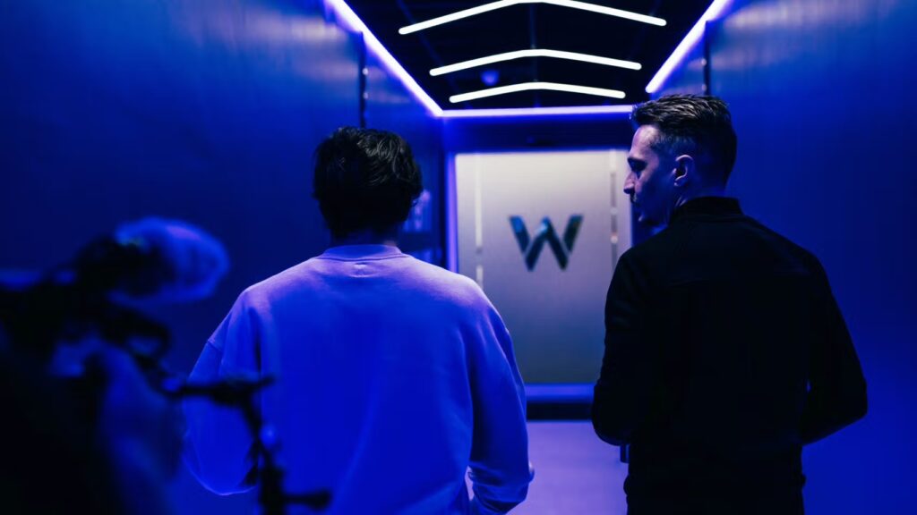 Back view of Carlos Sainz walking down corridor towards the Williams Racing logo